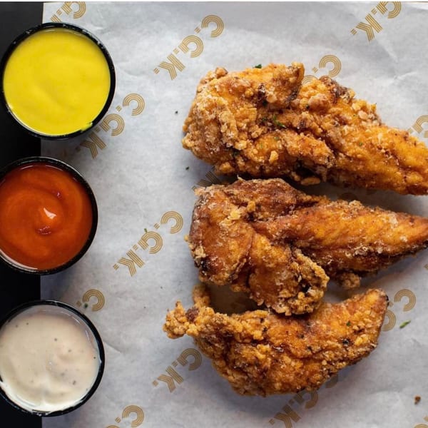 Three crispy fried chicken tenders with yellow, red, and white dipping sauces on branded paper.
