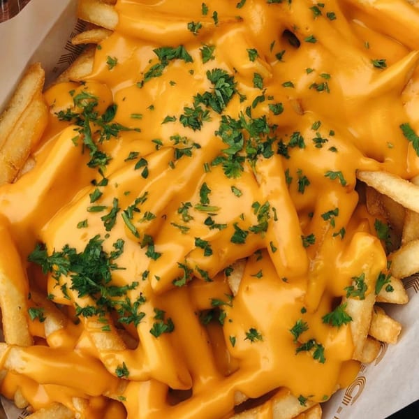Golden french fries generously covered in melted cheese sauce and sprinkled with fresh parsley.